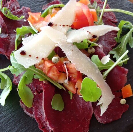 Carpaccio di cervo carpaccio di cervo guarnito con rucola, pomodorini, pepe verde, scaglie di grana e aceto balsamico di modena igt invecchiato 6 anni